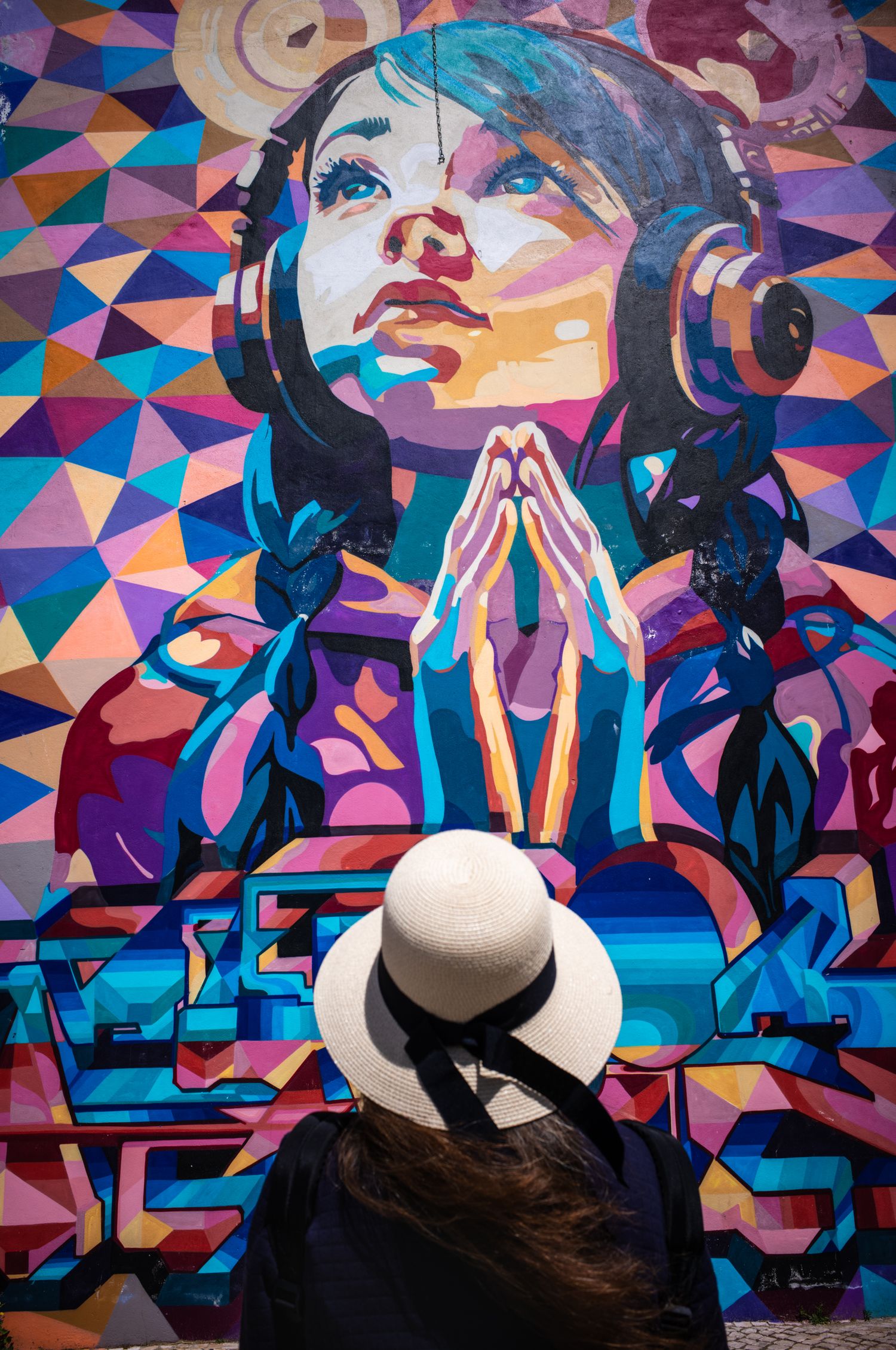 Woman in a white hat admires a vibrant mural at Lisbon's LX Factory, blending colorful street art with The Hat Series.