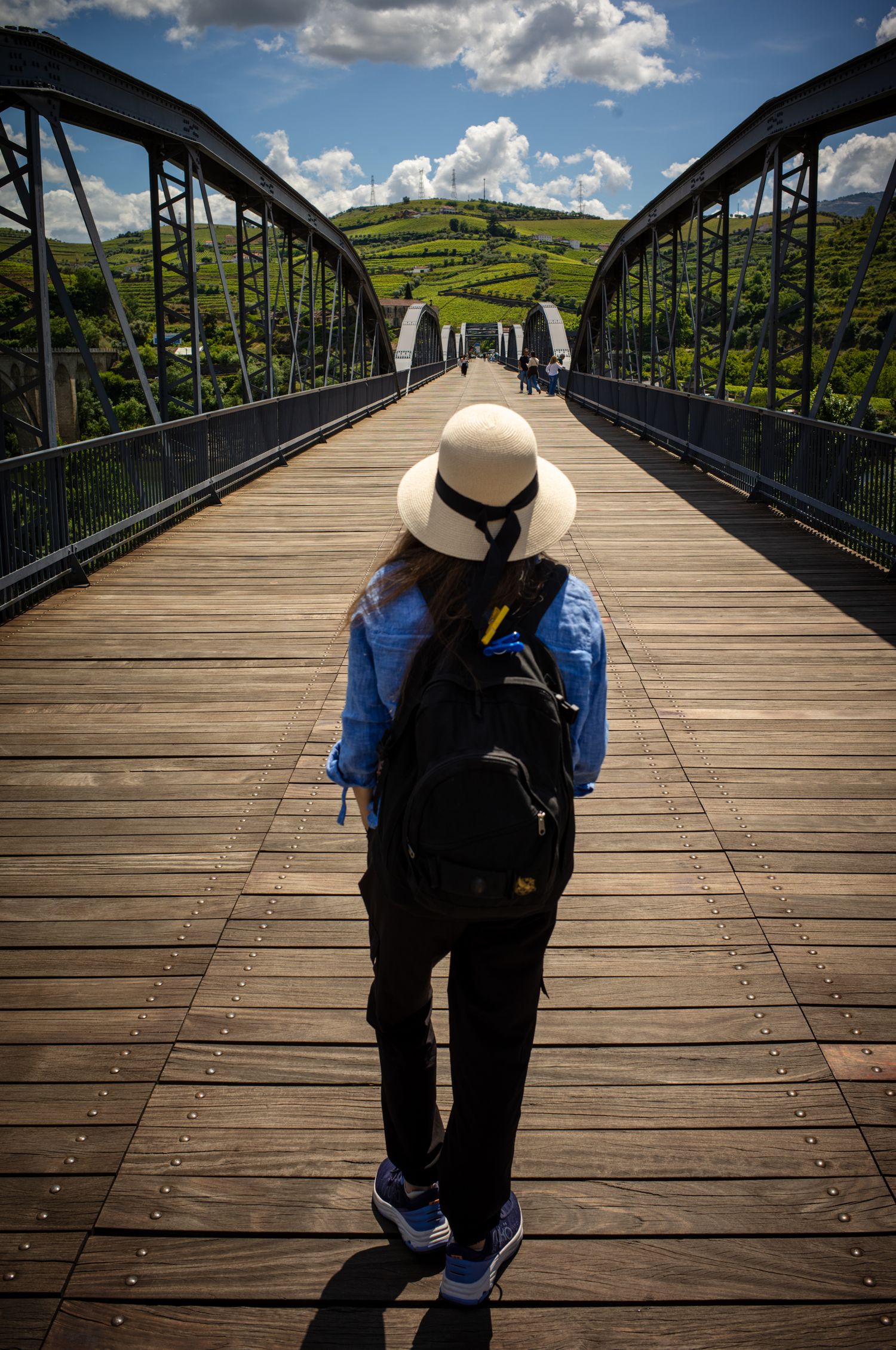 Woman in sun hat walking across Régua Pedestrian Bridge toward the Douro Valley vineyards in Peso da Régua, Portugal.