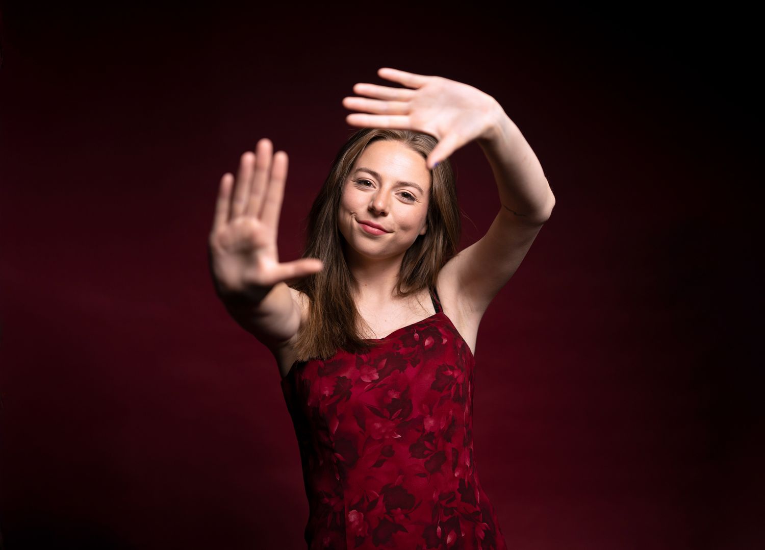 Young woman confidently frames the camera with her hands in a dramatic studio portrait against a deep red background.