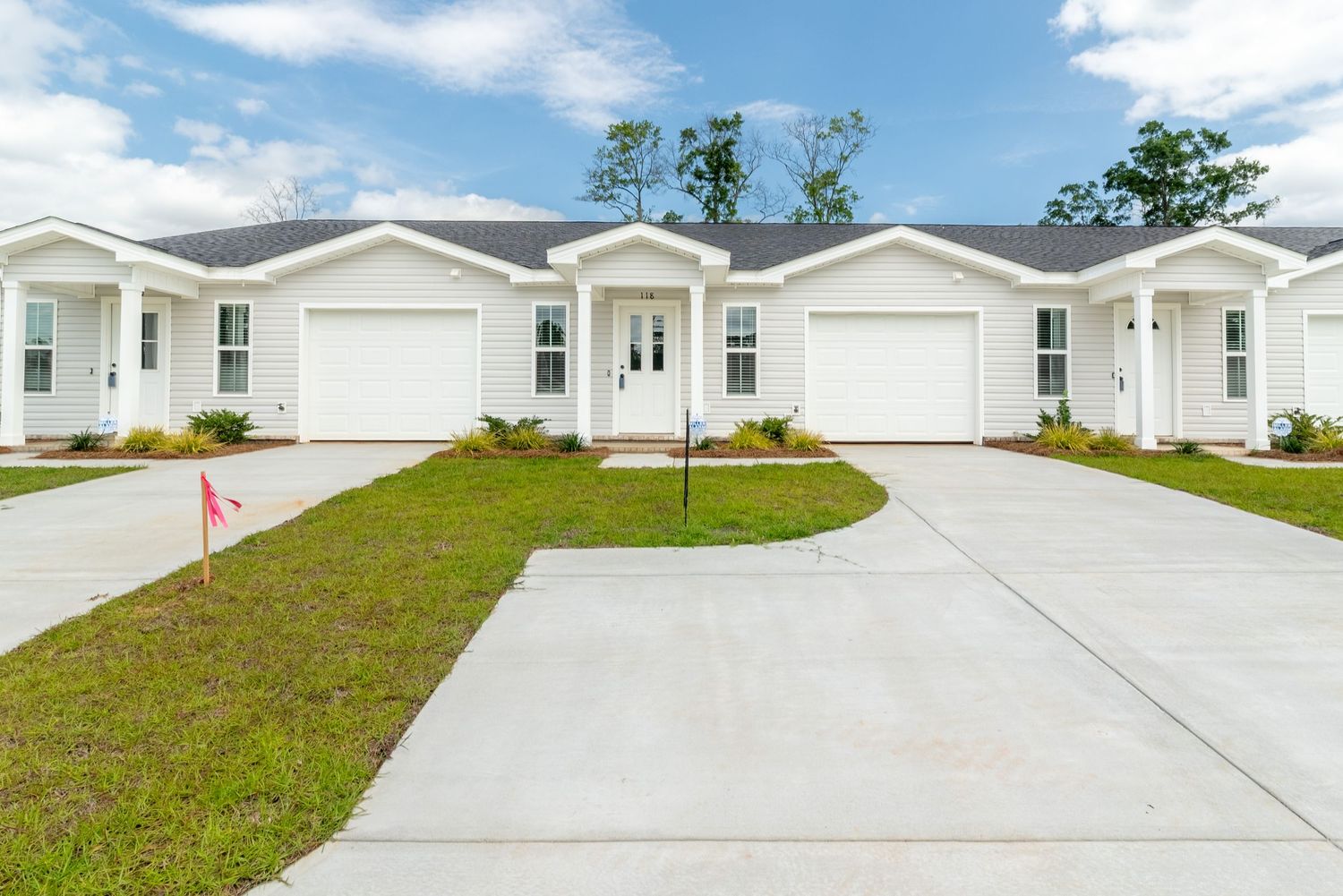 Row of single-story townhomes with garage, parking pad, and vinyl siding.