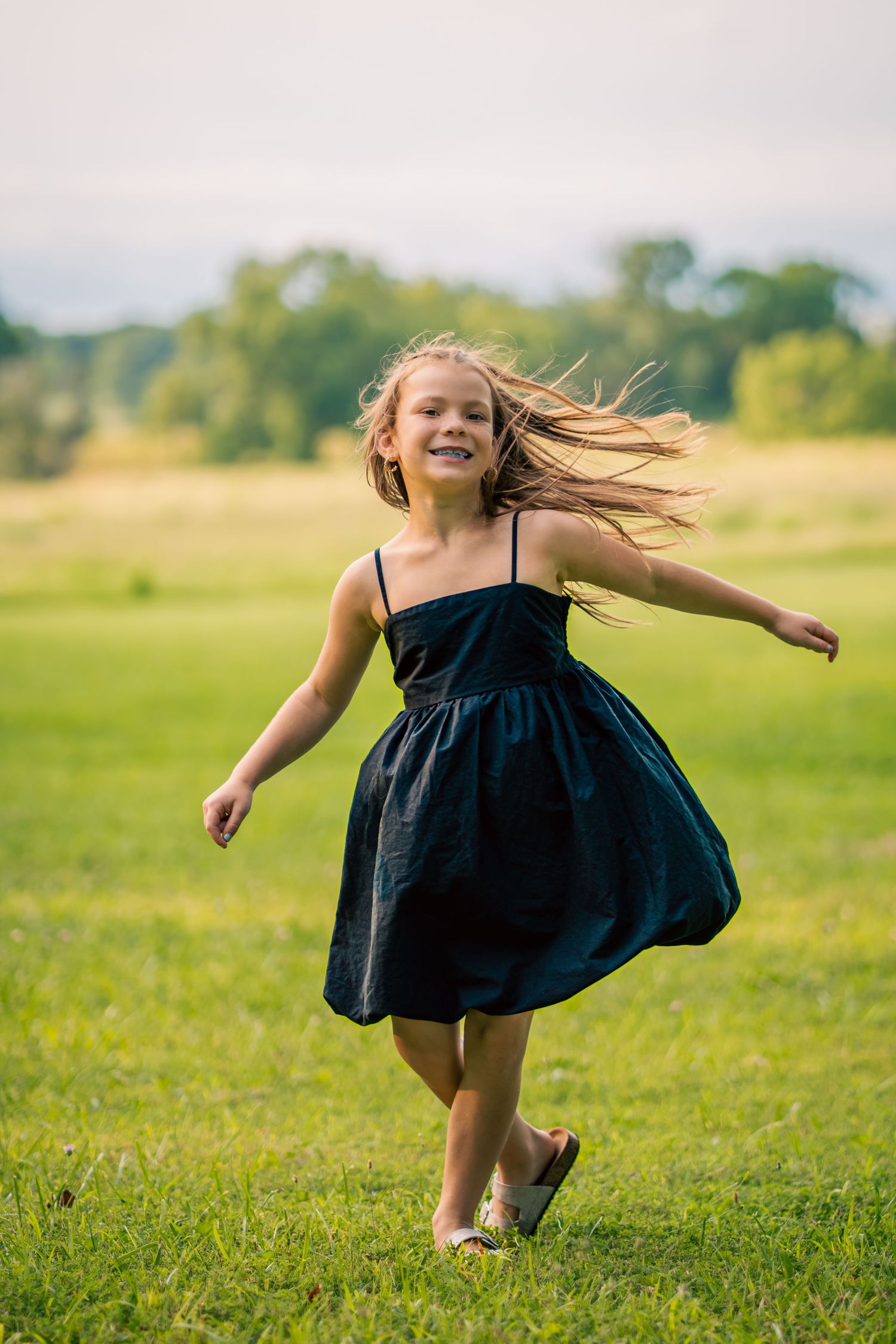 A joyful young girl in a black dress runs through a green field, her hair blowing in the wind.