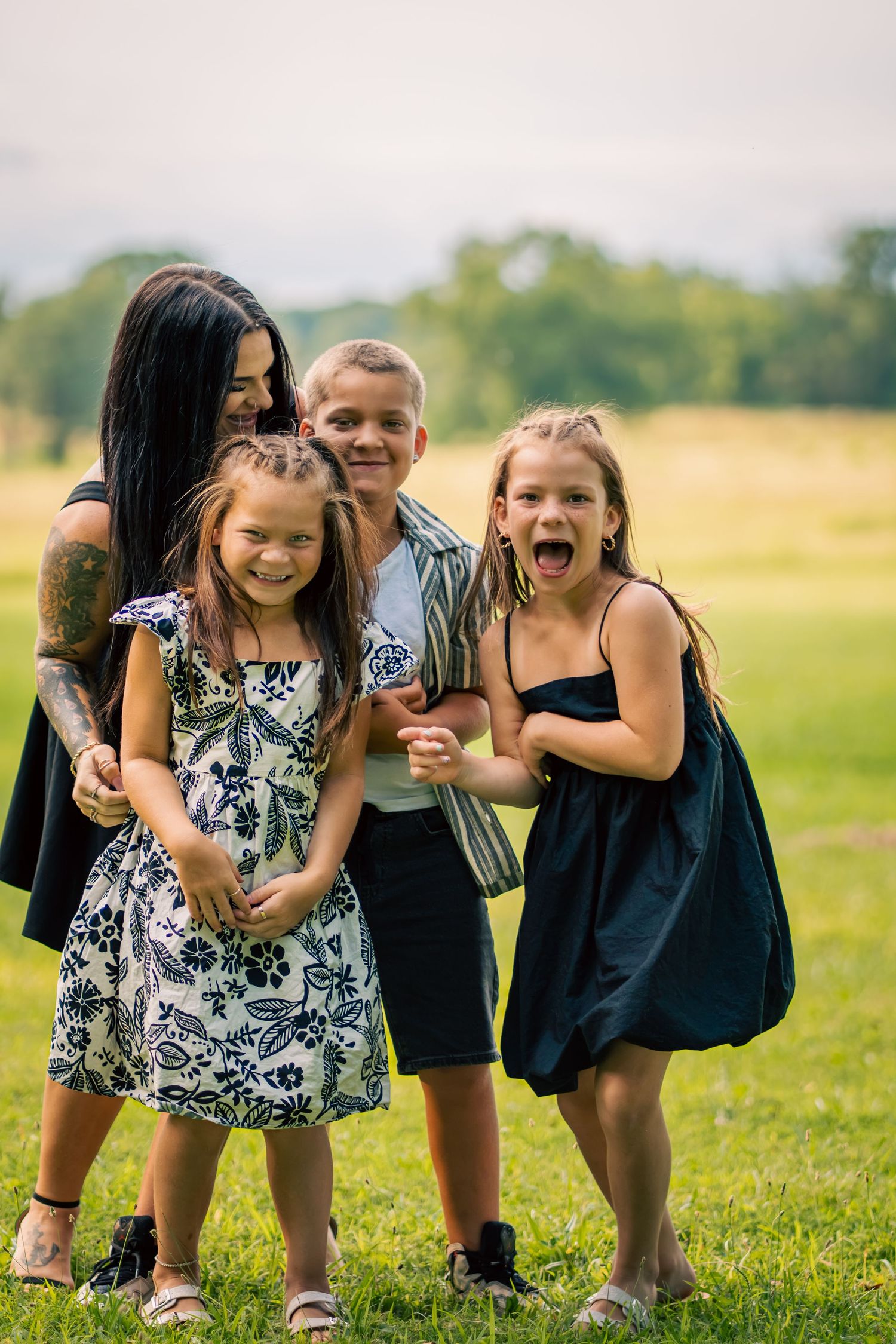 A woman and three children smiling and laughing together outdoors on a green grassy field.