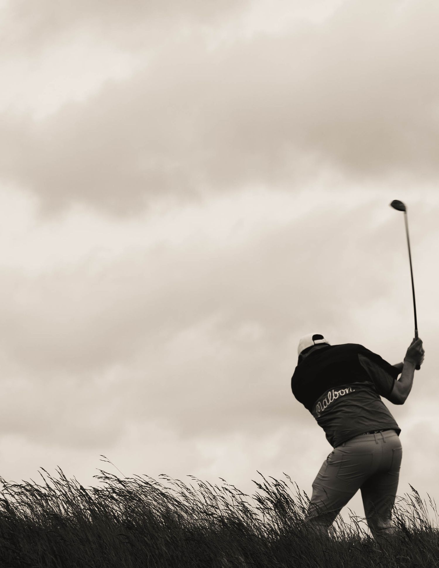 Black and white image of golfer mid-swing in long coastal grass