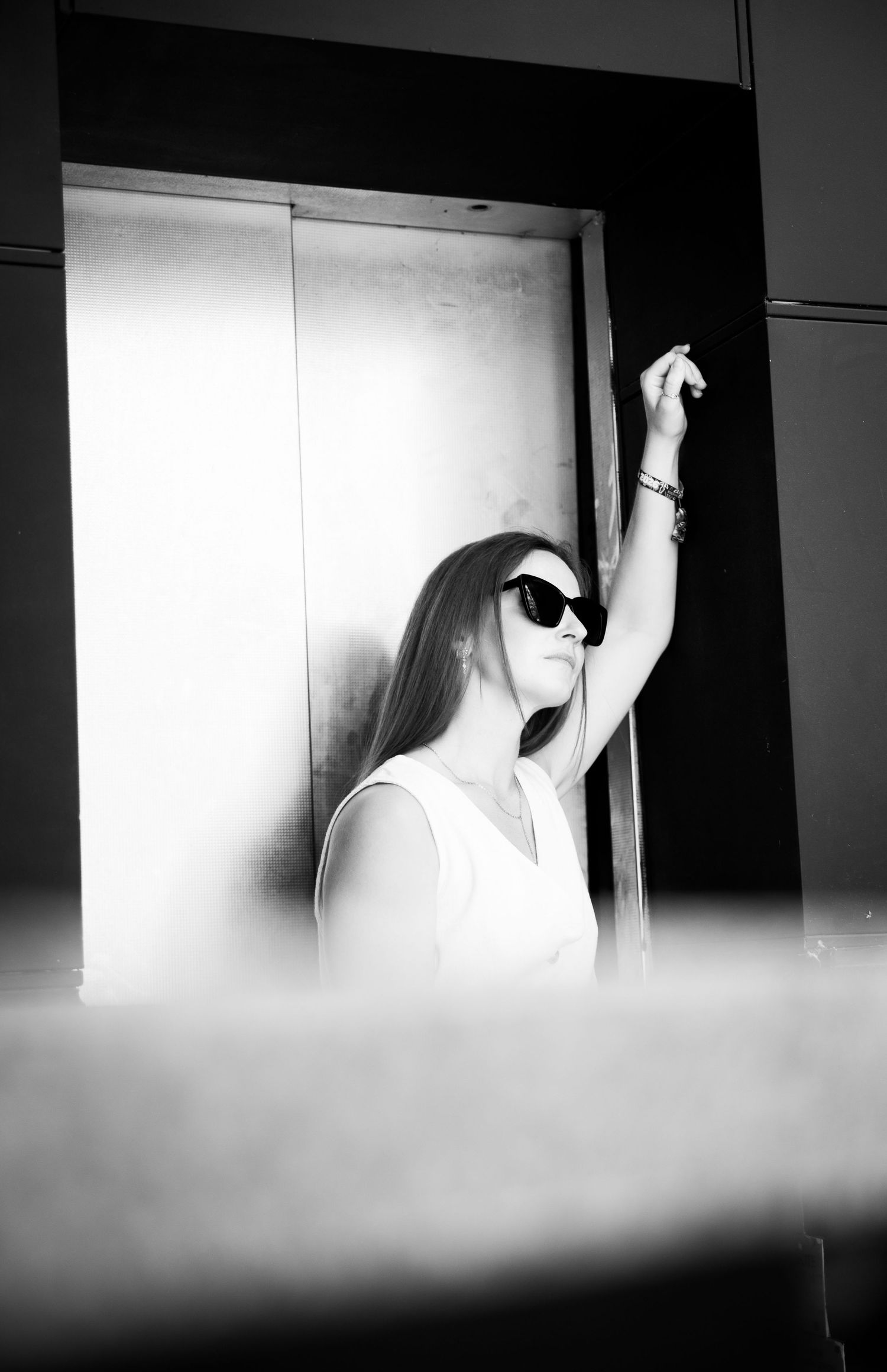 Black and white street portrait of woman in sunglasses leaning against elevator, urban portrait photography by James Gardner London