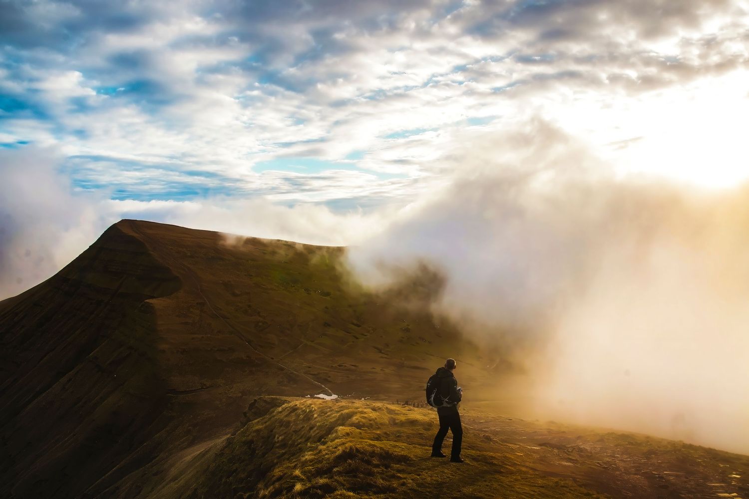 Photographer standing on Welsh mountain ridge as clouds roll in at golden hour, landscape photography by James Gardner