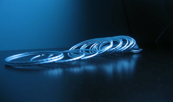 Colour photo of a set of silver bangles on a black table, lit with a blue light.