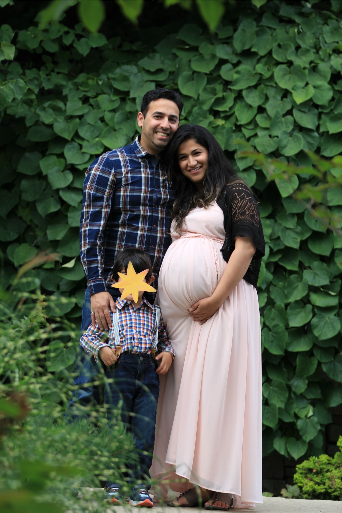 Photo of a couple, where one partner is heavily pregnant and holding her belly, as their young son stands in front of them.