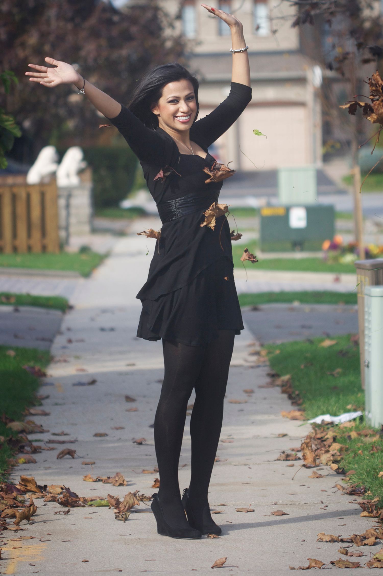 Photo of a standing young woman with her hands up in celebration as Autumn leaves dance around her.
