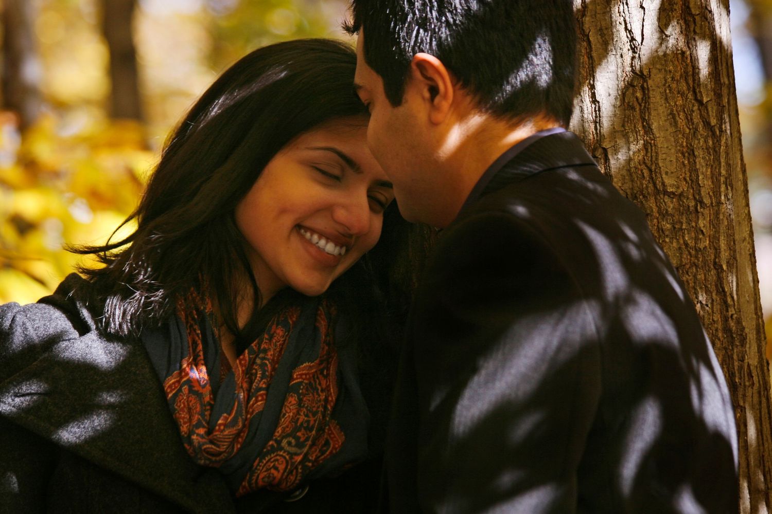 Photo of a young couple, with one partner looking down at their partner away from the camera, and the other shly closing their eyes.