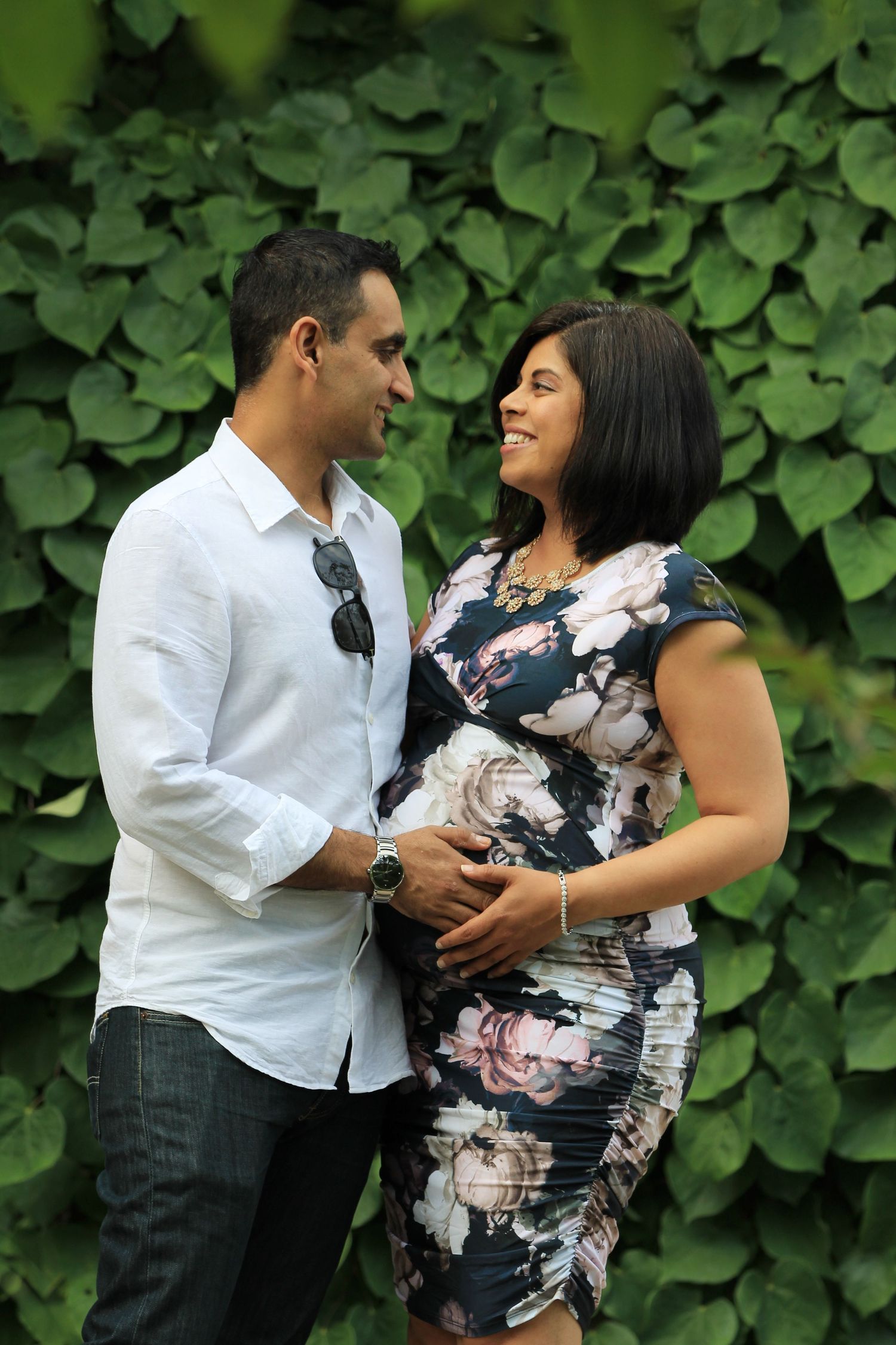 Photo of a couple looking adoringly at one another, as one partner holds their pregnant partner's belly.