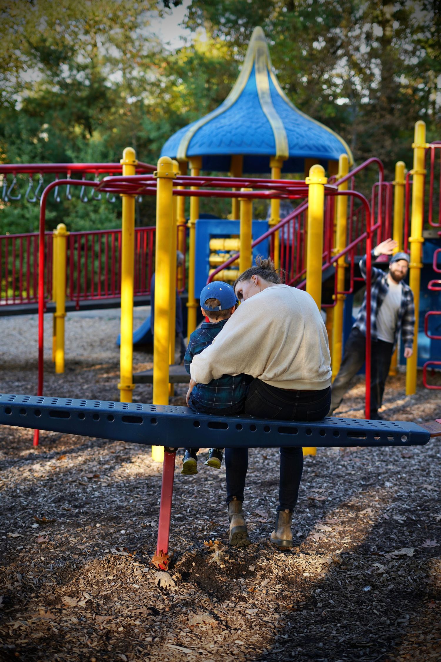 Photo of a young mother and her son from behind sitting on a park bench.