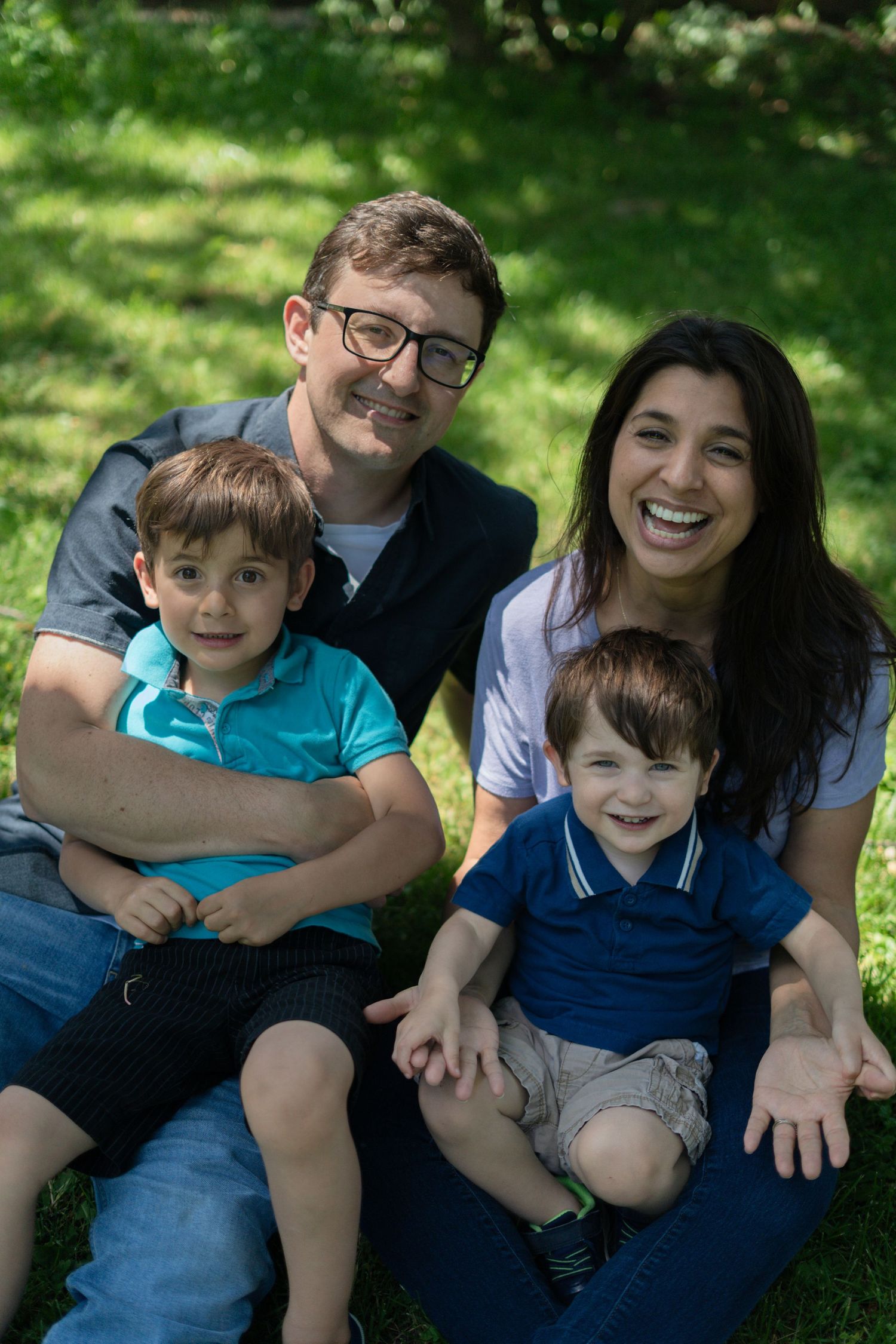 Photo of a family of four, sitting on the grass, laughing and smiling at the camera.