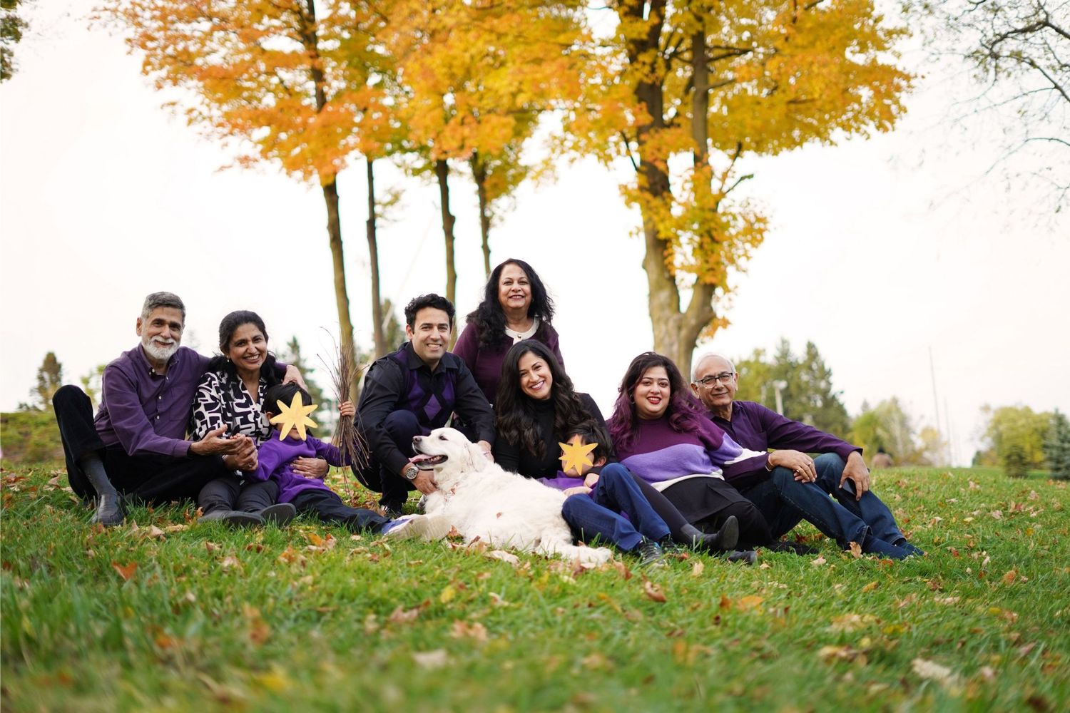 Photo of a large multigenerational family and their dog sitting on the grass in the Autumn time.
