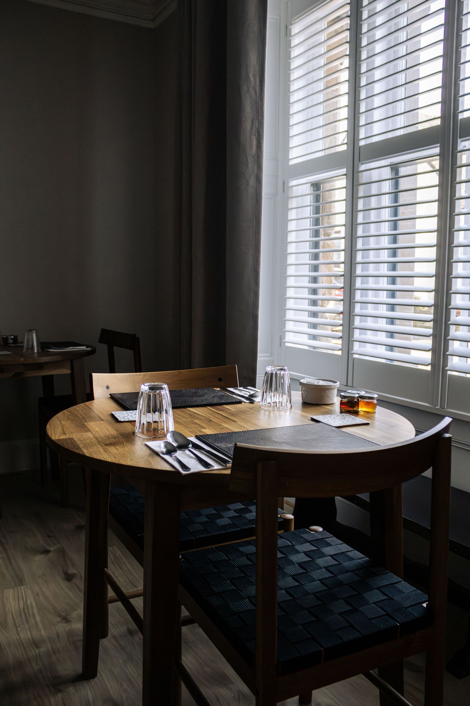 Elegant restaurant dining table set with glassware and menus near a bright window with white shutters.
