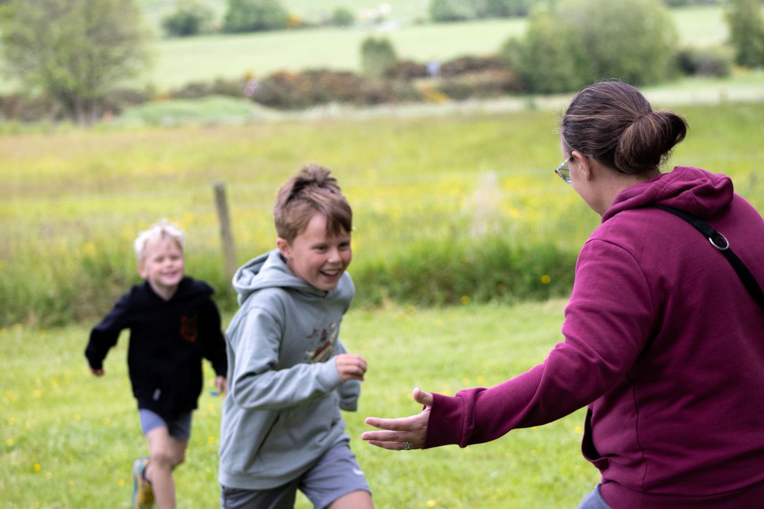 Children play and run together in a sunny green field outdoors.