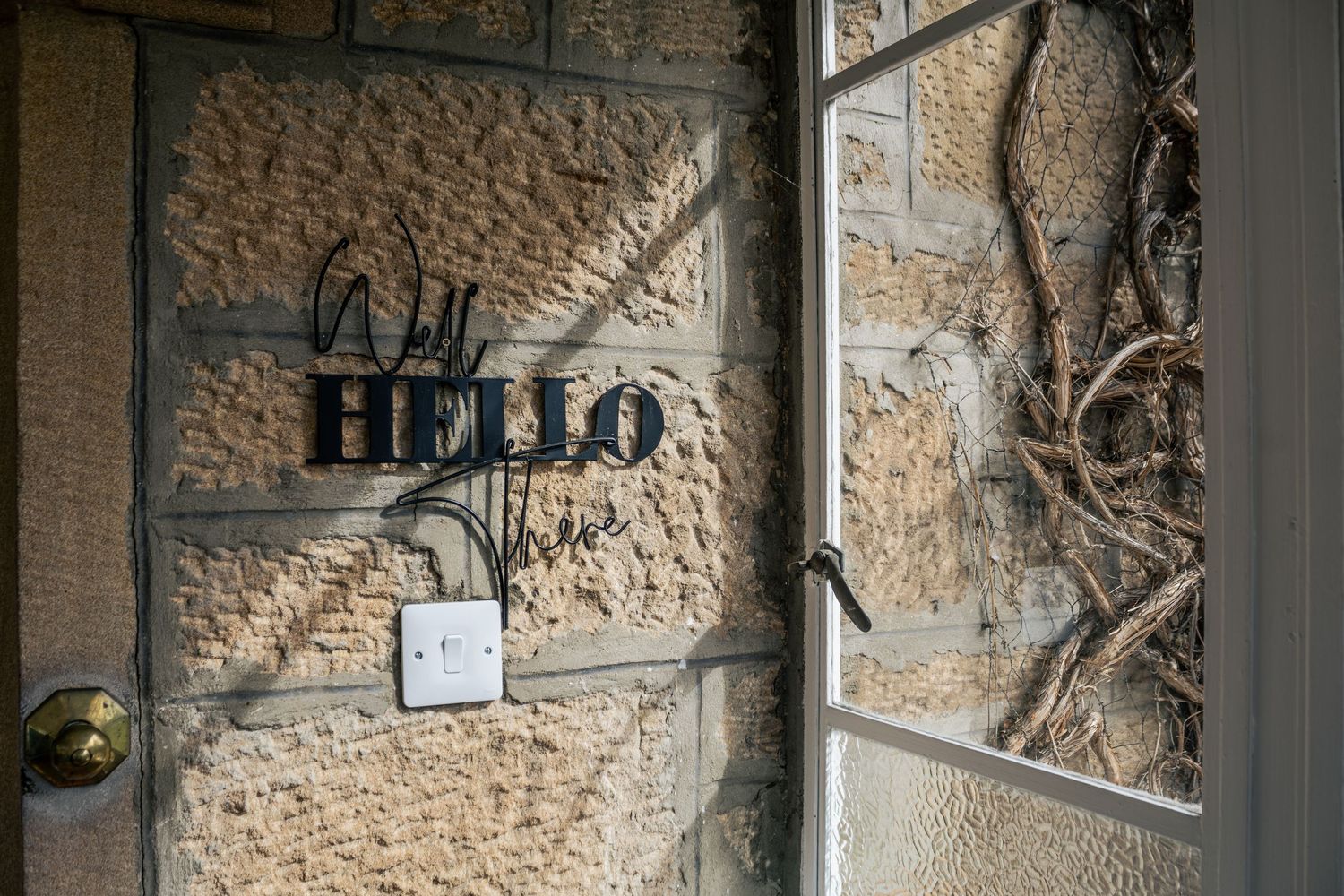 Stone wall with a decorative HELLO sign beside a glass door with climbing vines, creating a welcoming entrance.