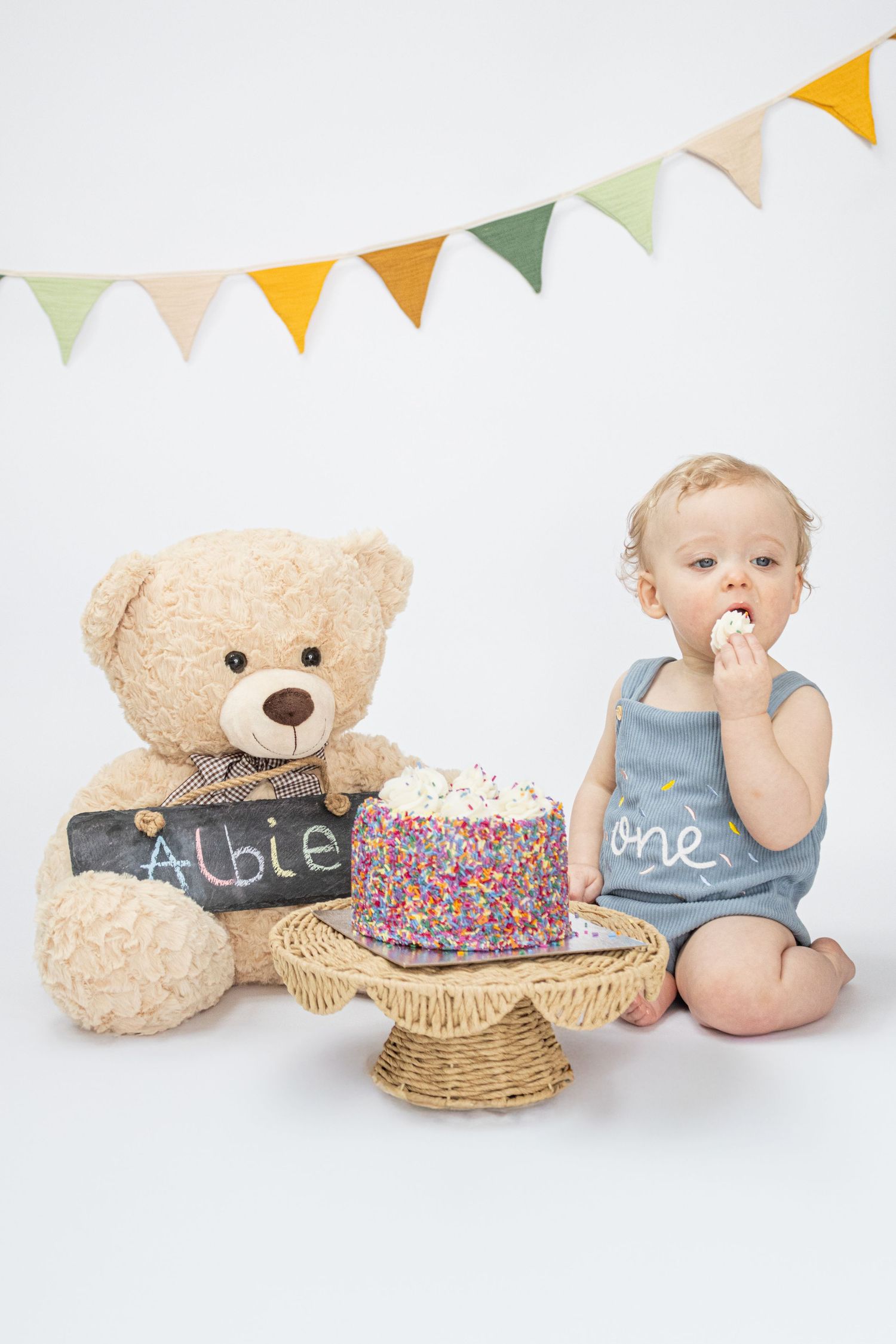 Baby boy Albie celebrates his first birthday with a sprinkle cake and teddy bear at a cake smash photoshoot.