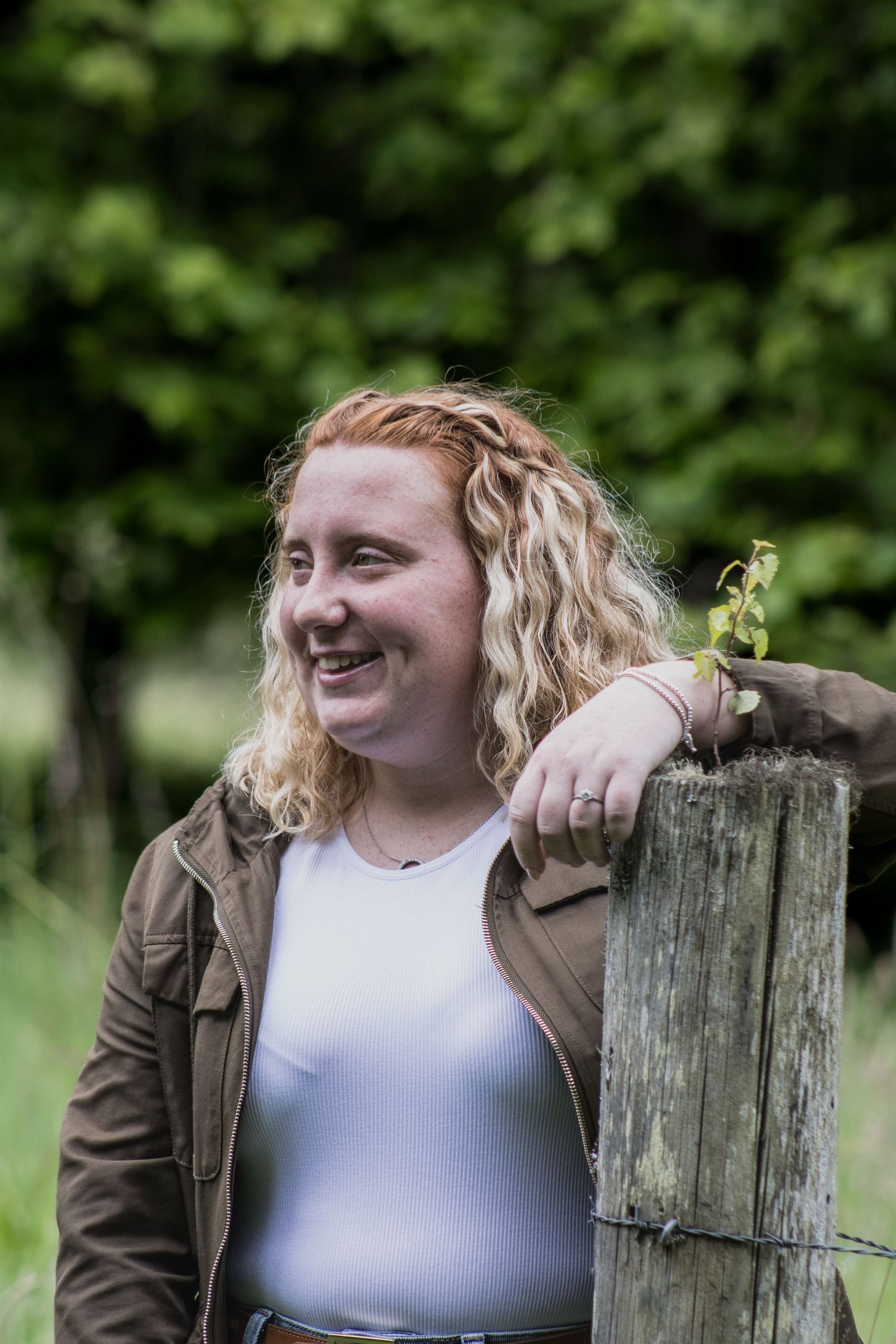Person in brown jacket interacts with small bird perched on wooden fence post.