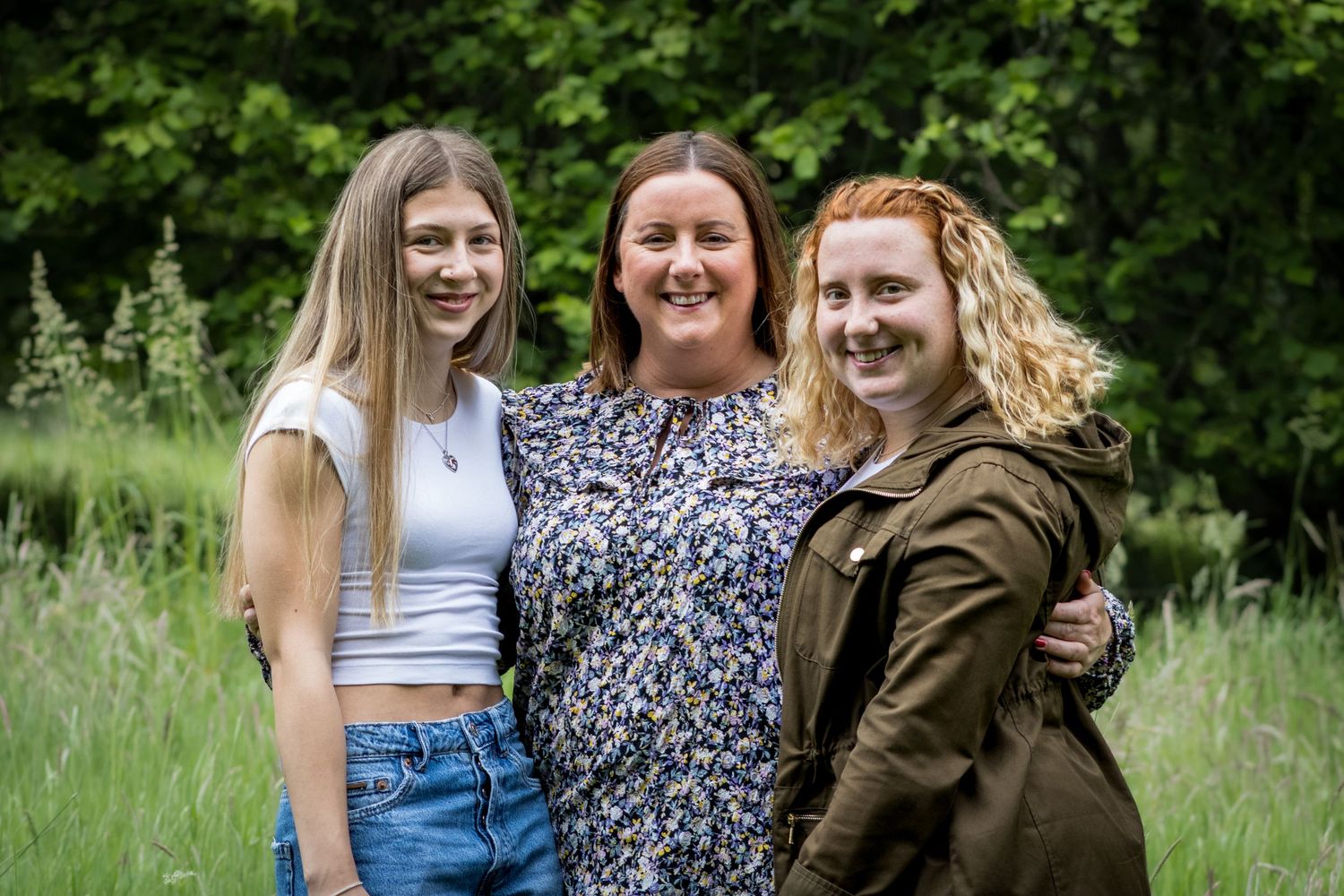 Three friends pose together in a meadow wearing casual summer clothing.