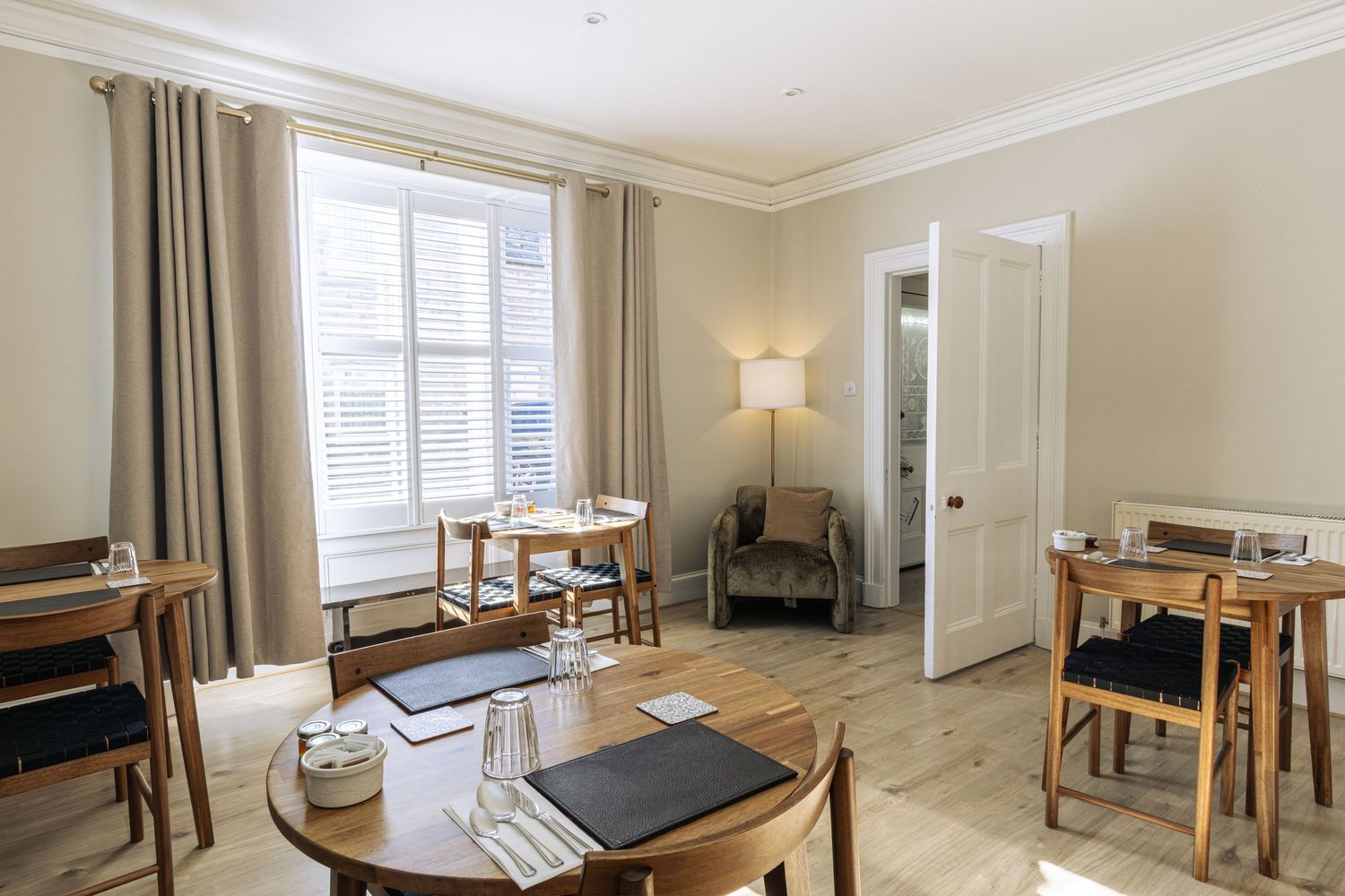 Bright, elegant living and dining area with neutral tones, wooden furniture, large windows, and warm lighting.