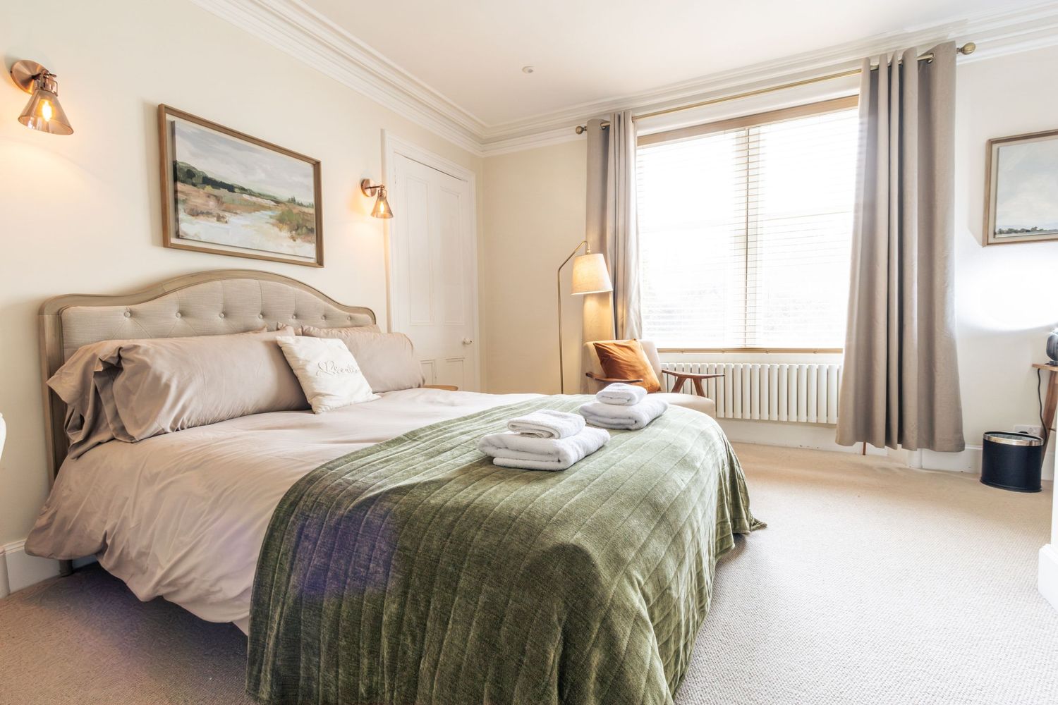 Elegant bedroom with tufted headboard, green velvet throw, white bedding, neutral decor, and a bright window with curtains.
