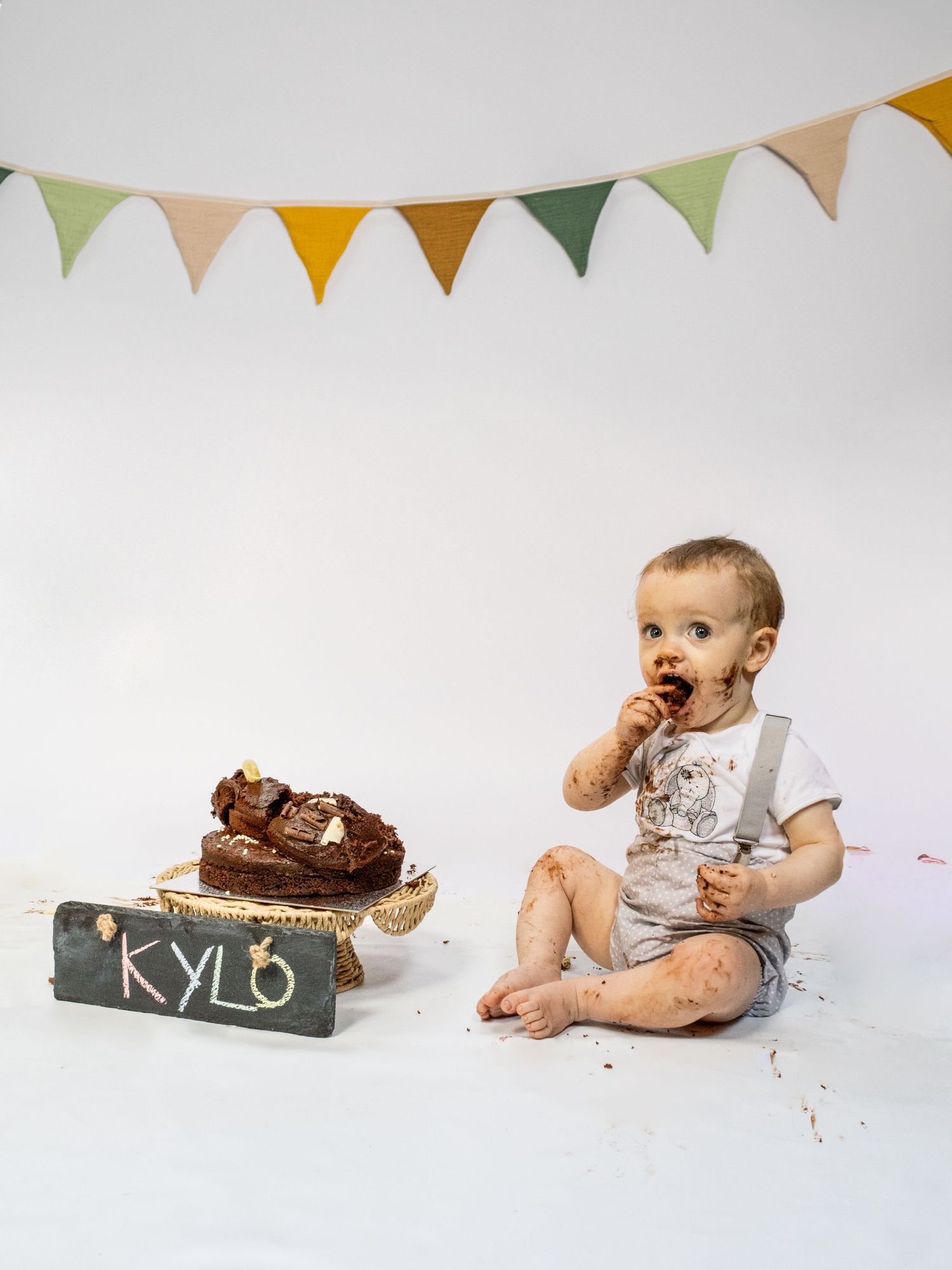 Baby Kylo covered in chocolate cake celebrating first birthday with bunting banner and smashed cake display.