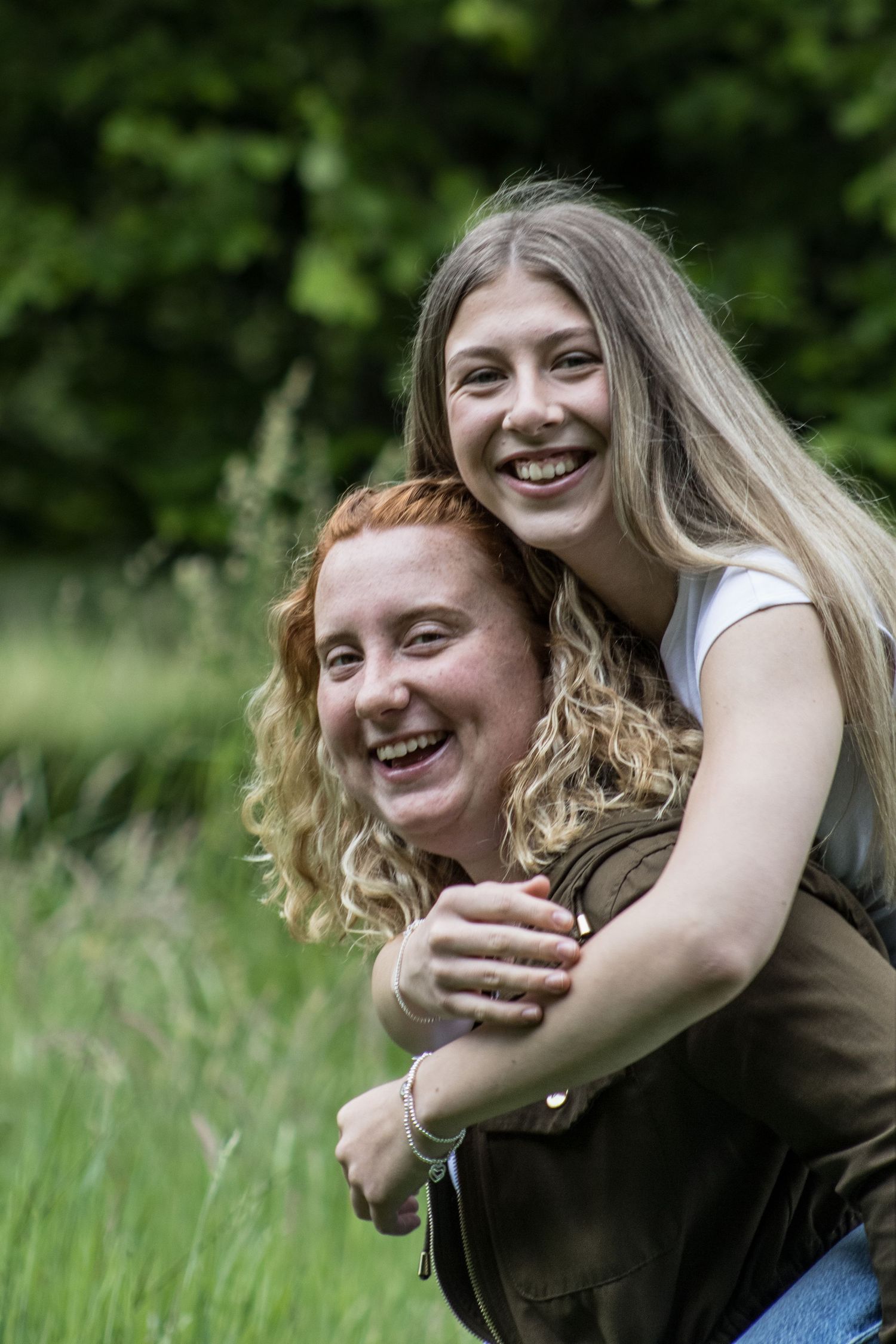 Two friends share a joyful piggyback moment in a sunny meadow with natural greenery.