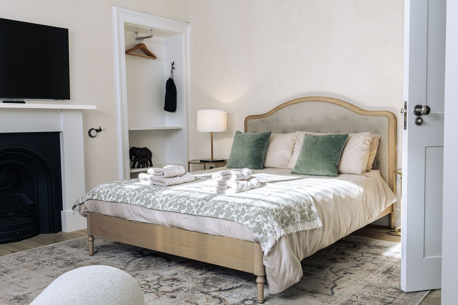 Elegant bedroom with a upholstered bed, green accent pillows, fireplace, and soft neutral decor on a patterned rug.