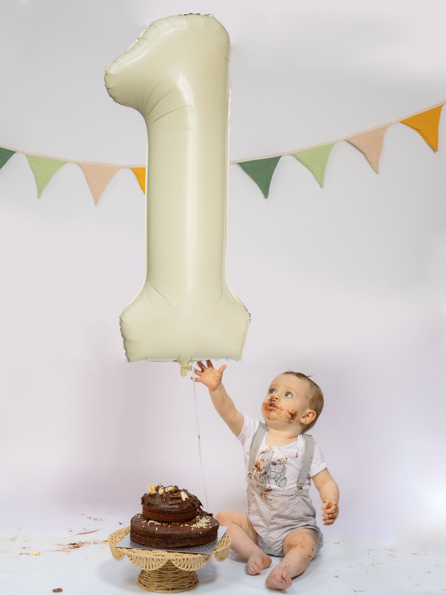 Baby's first birthday celebration with number one balloon and smashed chocolate cake on cake stand.