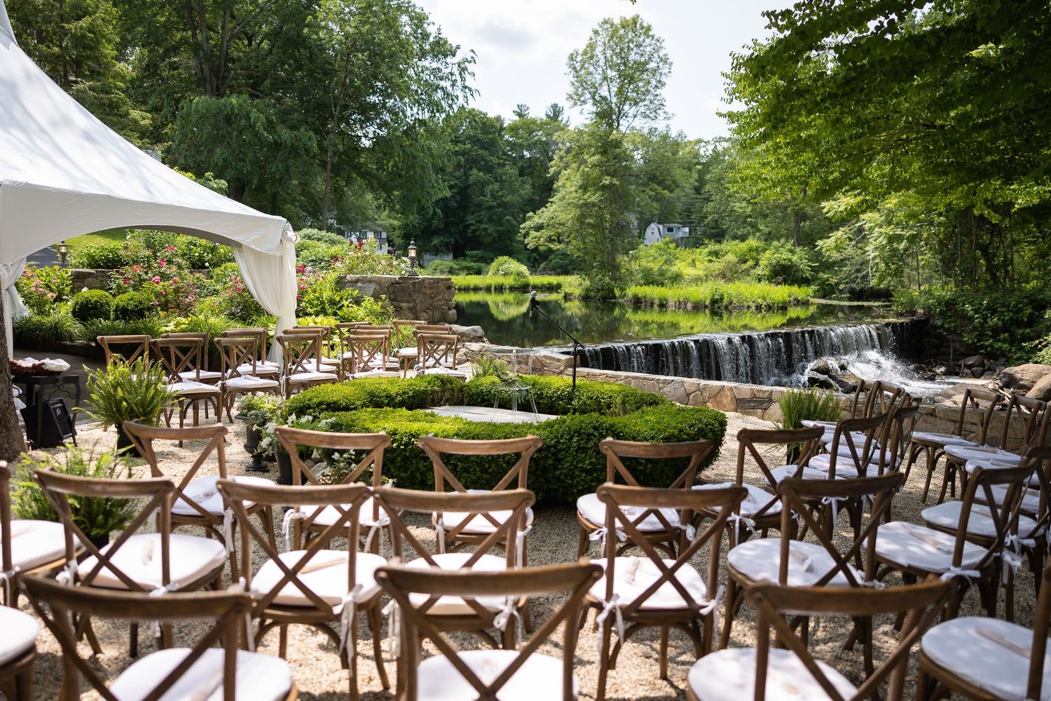 Outdoor wedding reception setup with rustic wooden chairs and white tent.