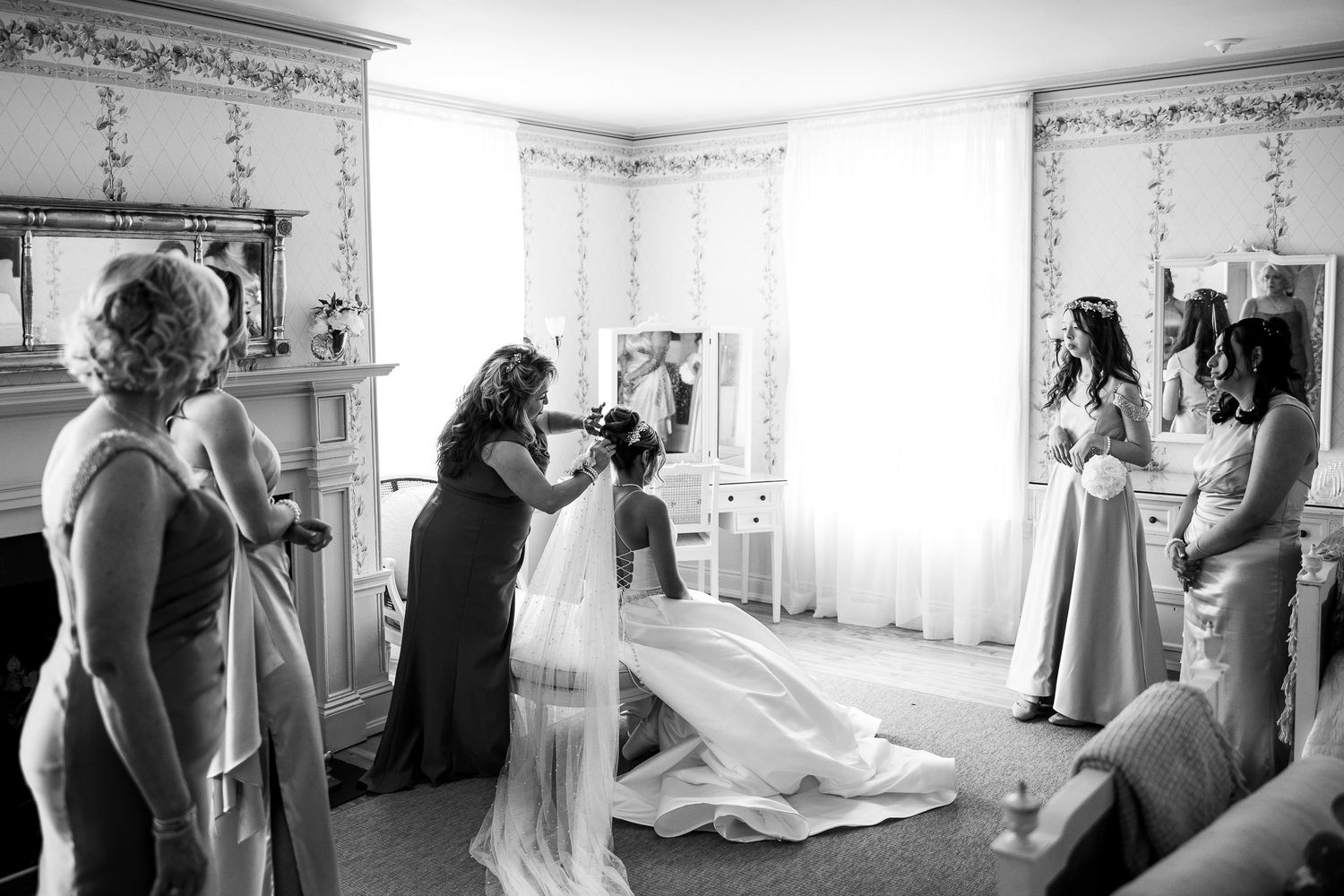 Black and white photo of wedding party getting ready in bright sunlit room.