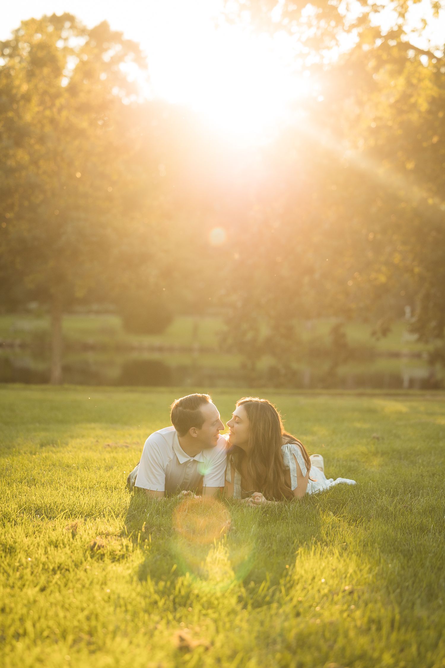 Couple lying on green grass sharing a romantic moment during golden hour sunset in a lush park.