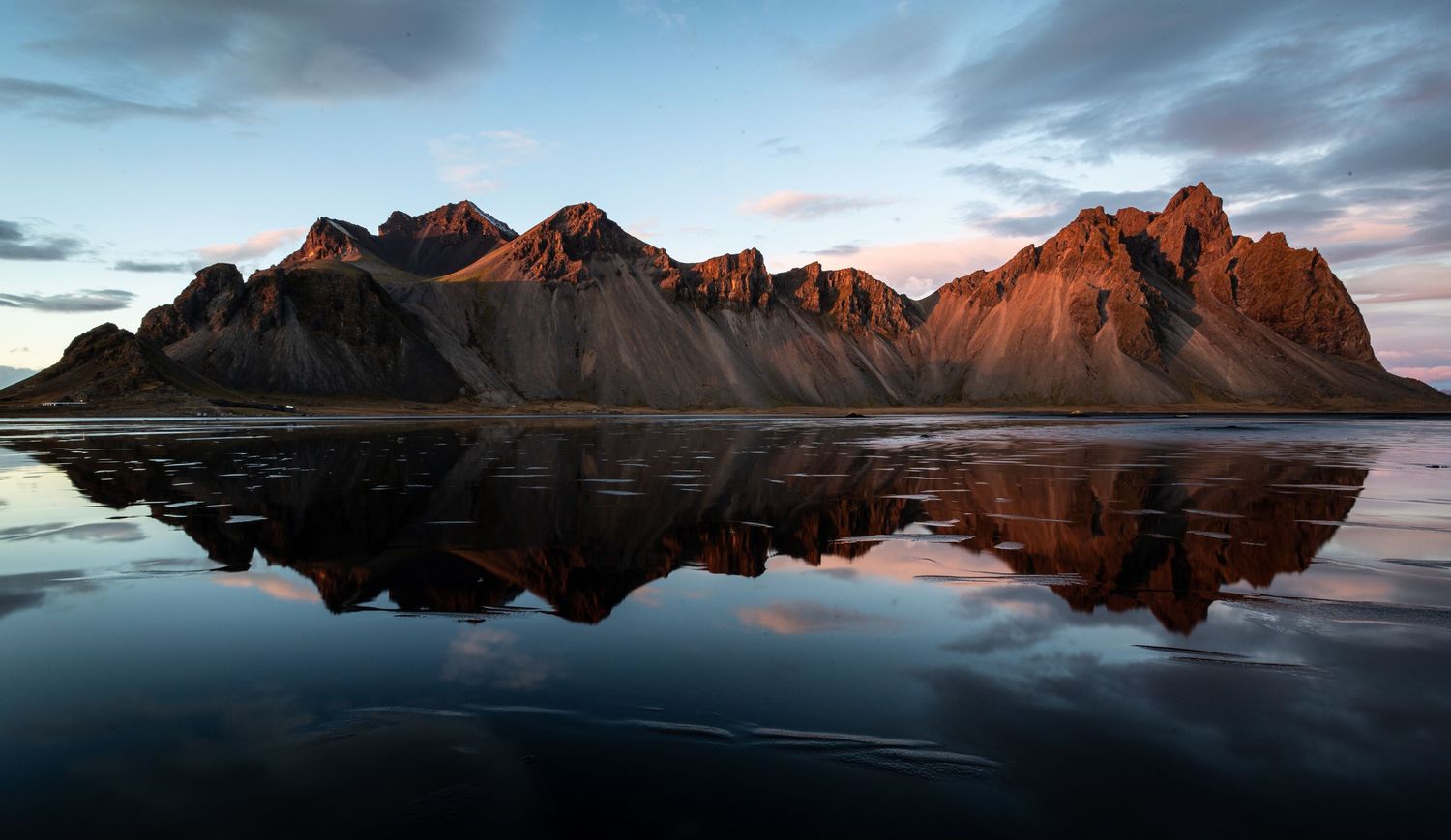 Mountain range reflecting perfectly in calm water during sunset with dramatic lighting.