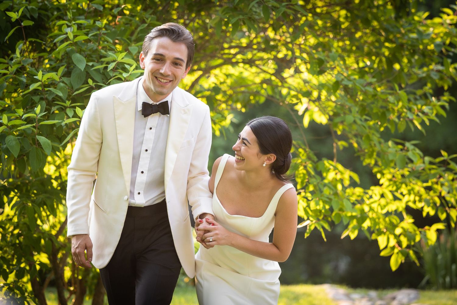 Wedding couple poses in a sun-dappled garden with golden light filtering through trees.