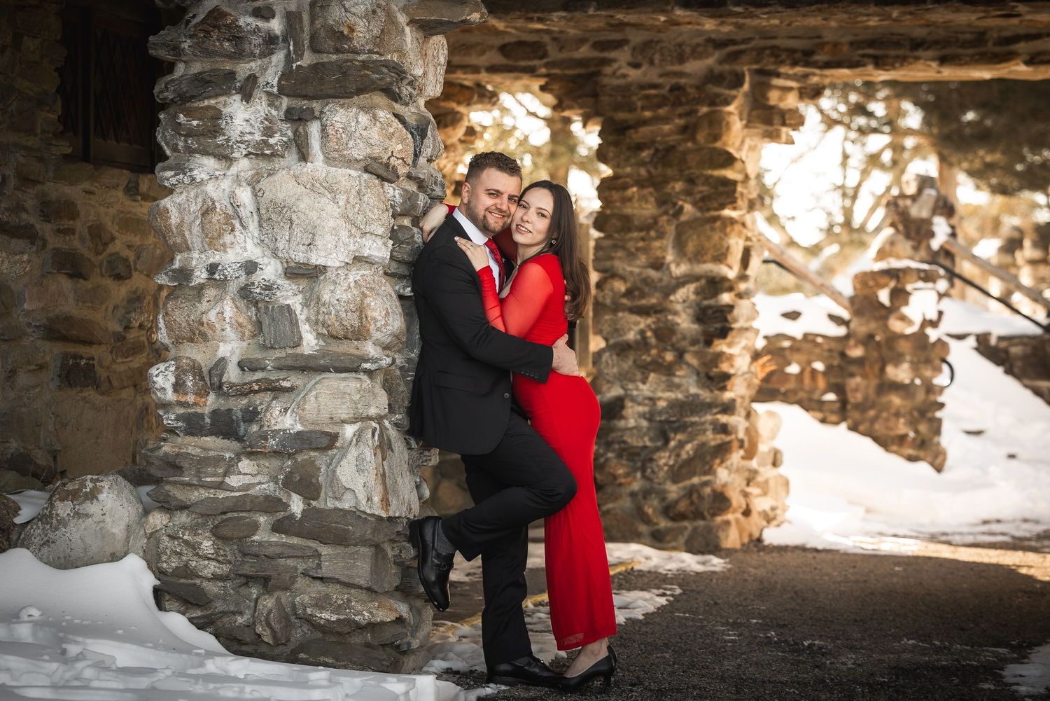 A romantic winter engagement photo session under a stone bridge with snow on the ground.