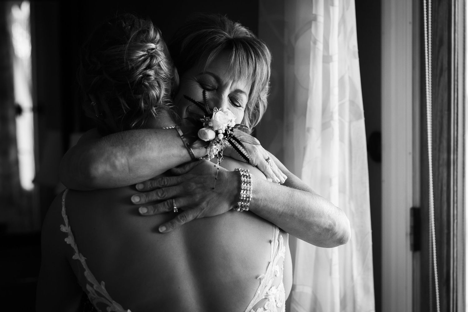 Black and white photo of a couple embracing in romantic silhouette against window light.