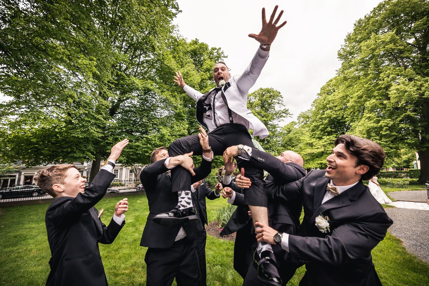 Wedding party members jumping and celebrating outdoors on a sunny day.