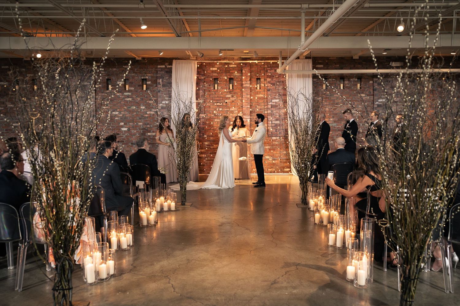 Rustic indoor wedding venue decorated with glowing candles and bare branches creating a romantic atmosphere.