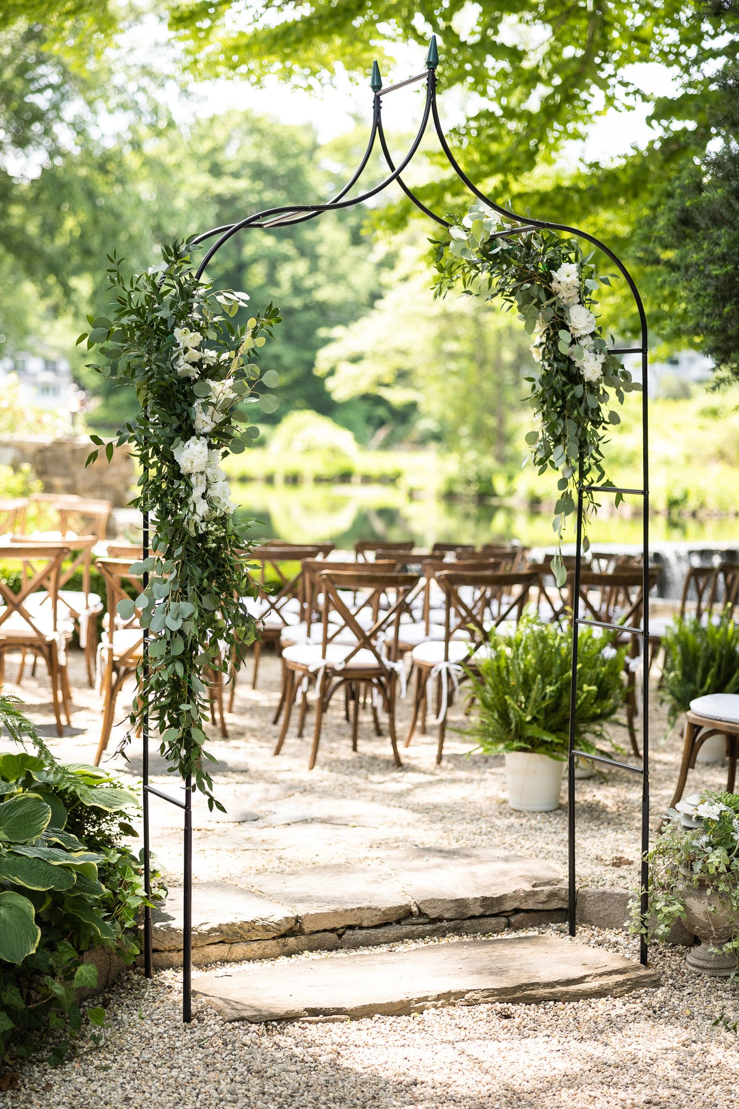 Garden ceremony aisle decorated with greenery and black metal arches.
