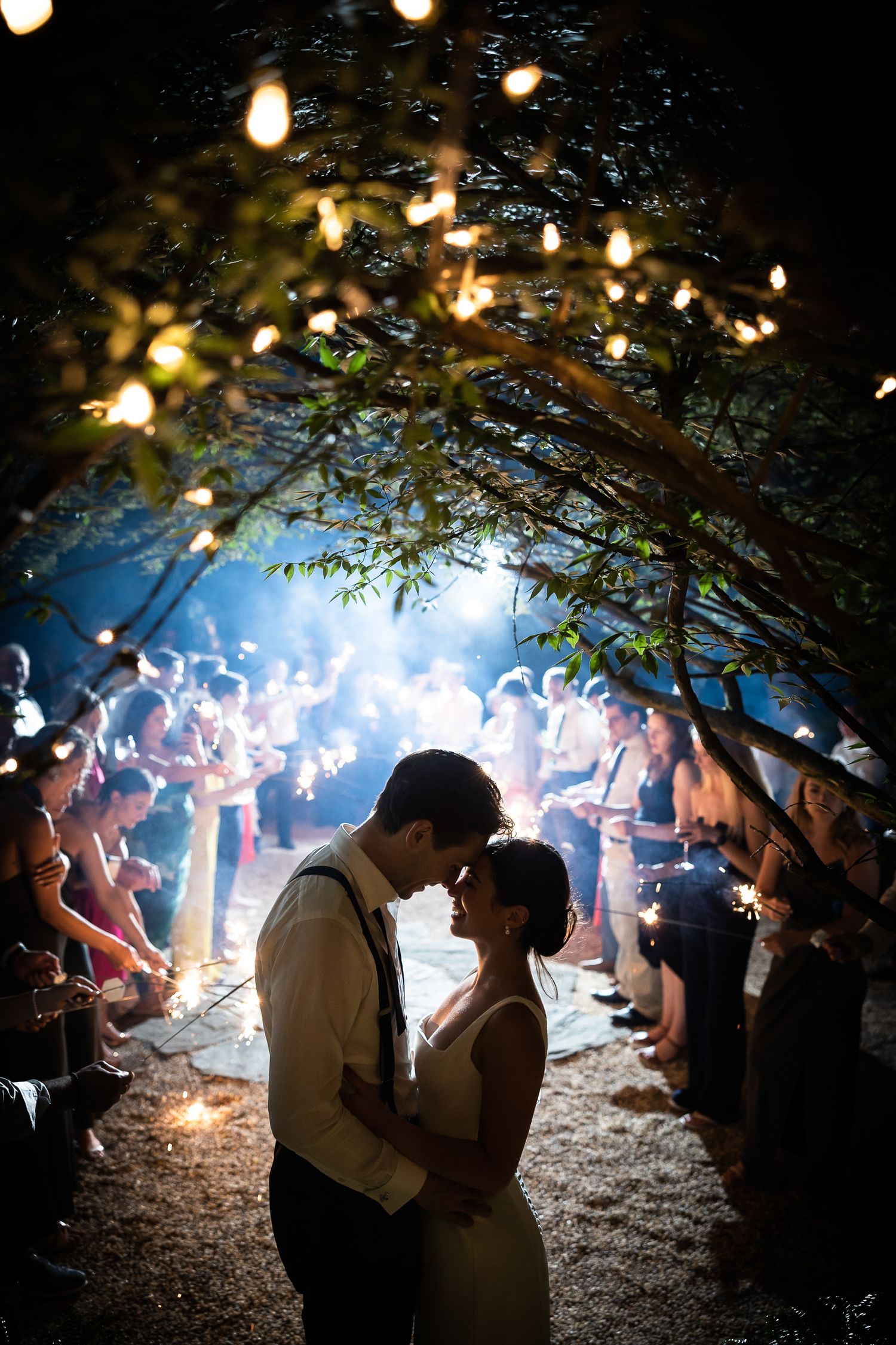 A romantic nighttime outdoor wedding celebration with string lights and sparklers creating a magical atmosphere.