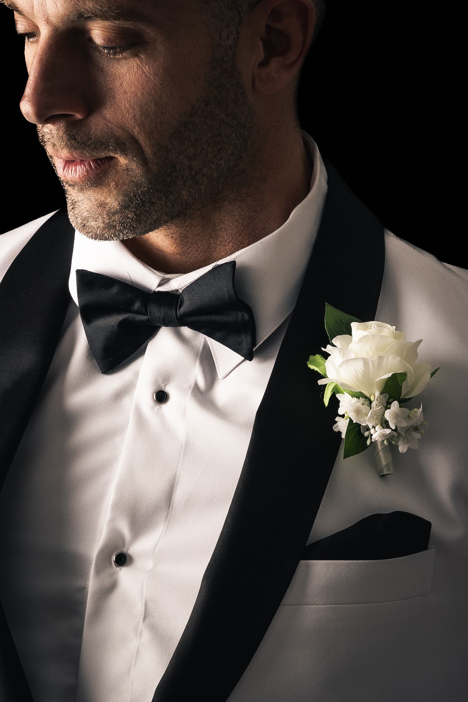 A black and white series of wedding attire details showing a bow tie, boutonniere and tuxedo lapel in dramatic lighting.