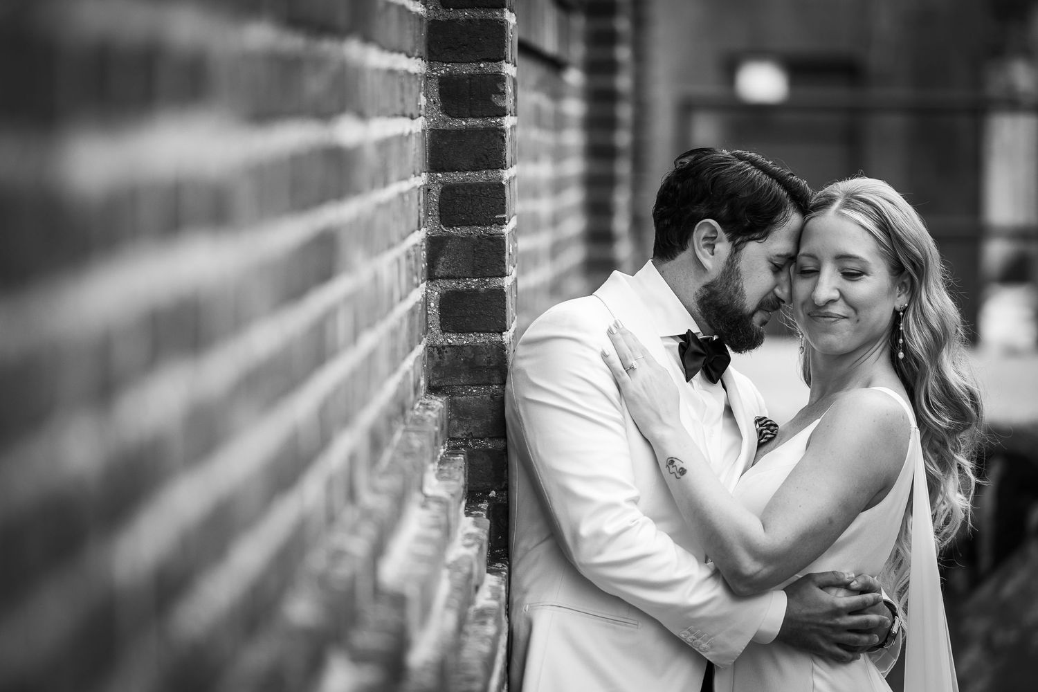 Black and white romantic couple portrait series showing intimate moments against a brick wall background.