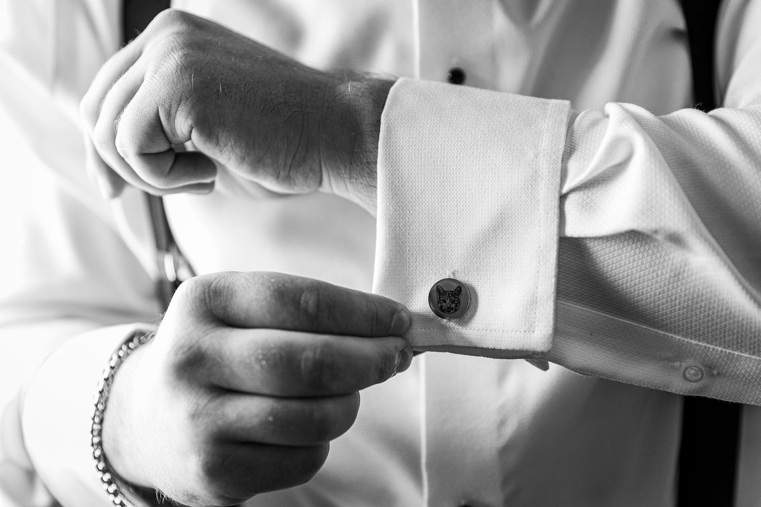 Close-up details of groom adjusting cufflinks and formal wear accessories.
