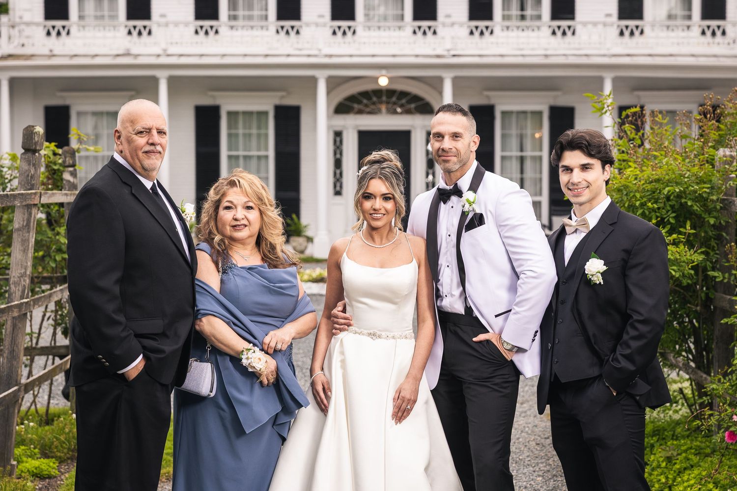 Wedding party members gather for formal photos on the grounds of a historic white mansion.