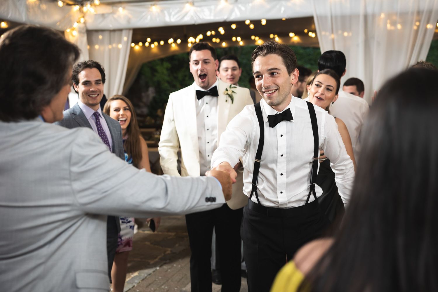 Wedding reception guests dancing and celebrating under twinkling lights and white drapes.
