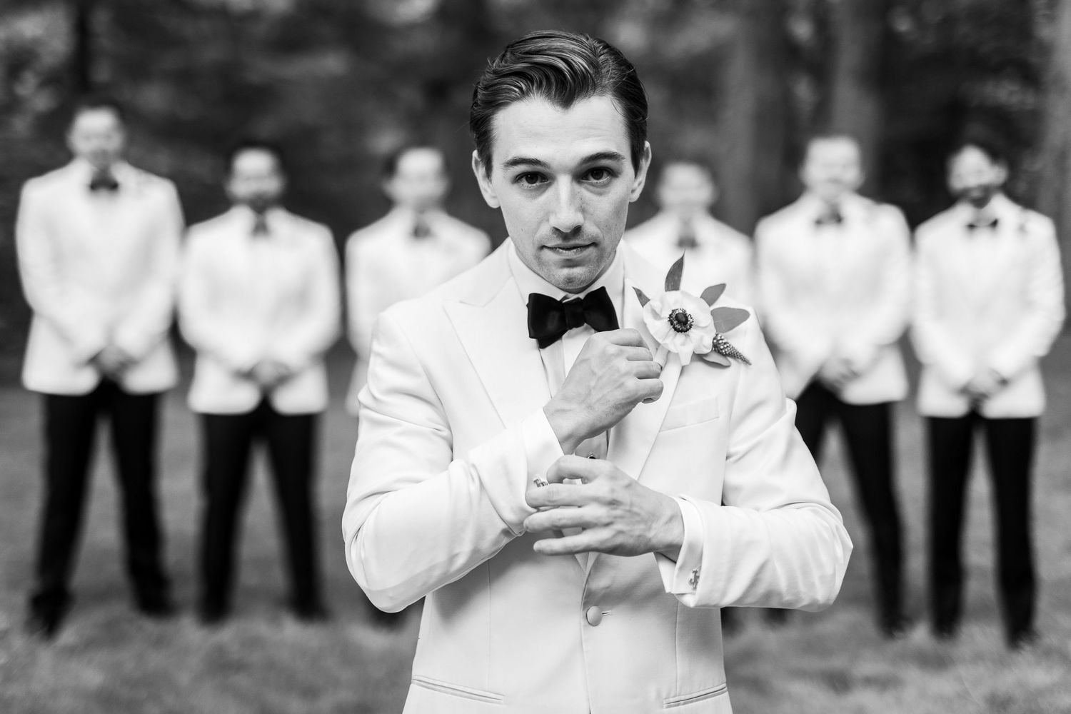 Groom adjusting cufflinks with groomsmen in the background.