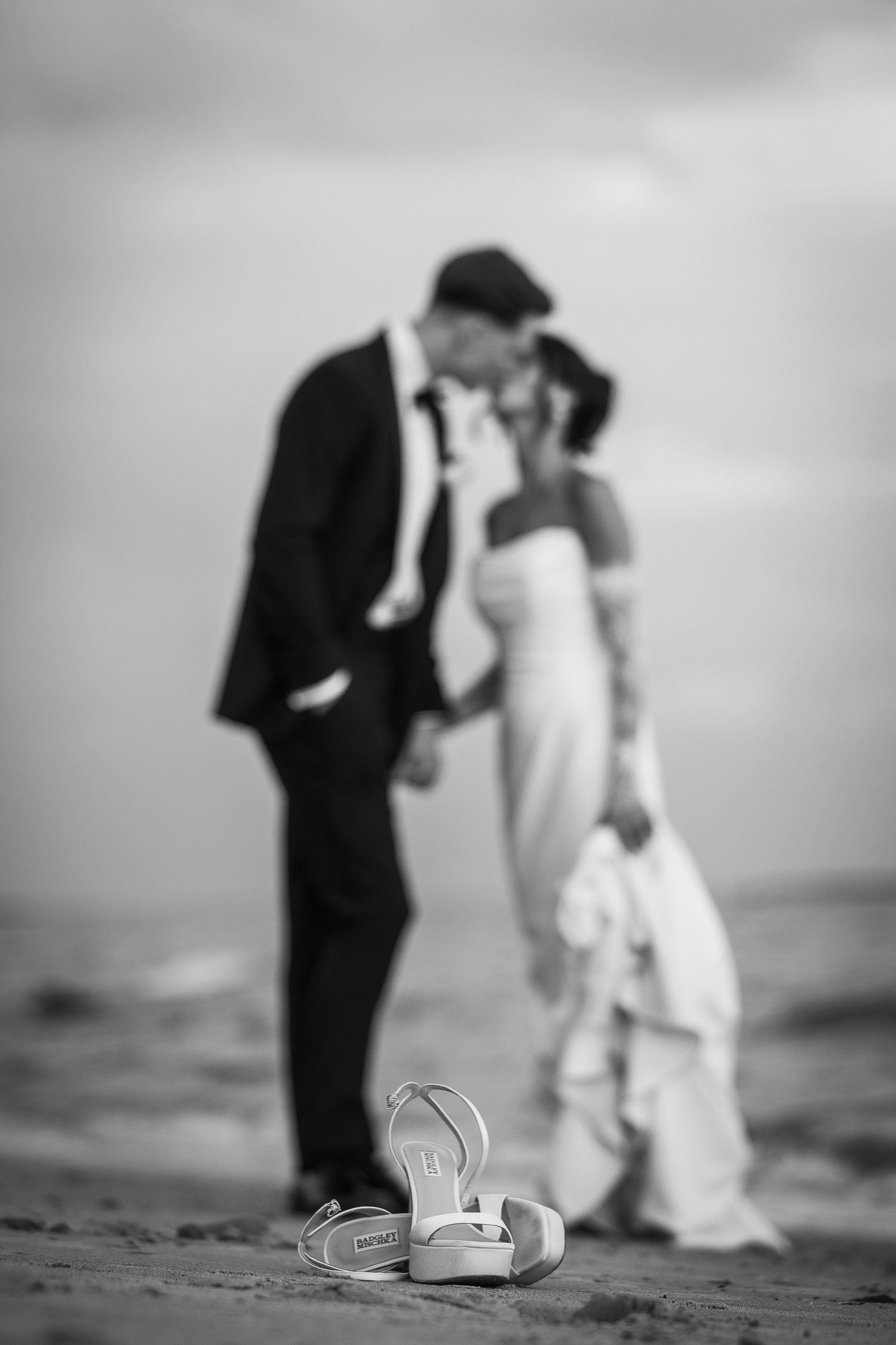 Wedding couple poses intimately on a beach with shoes in foreground.