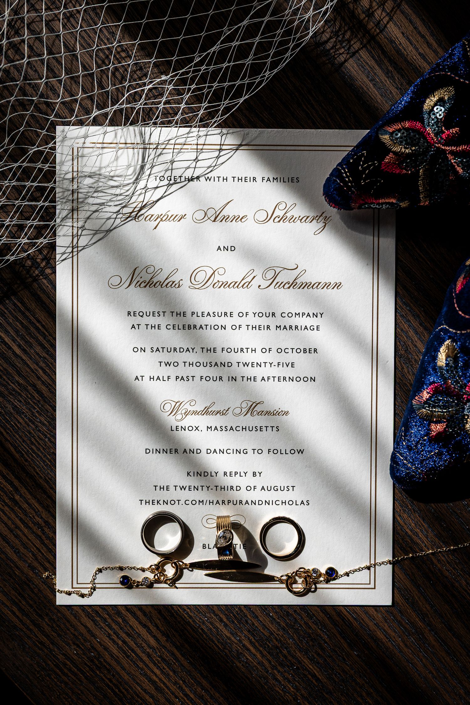 Elegant wedding invitation suite with rings and calligraphy text displayed on dark wooden surface with decorative details.