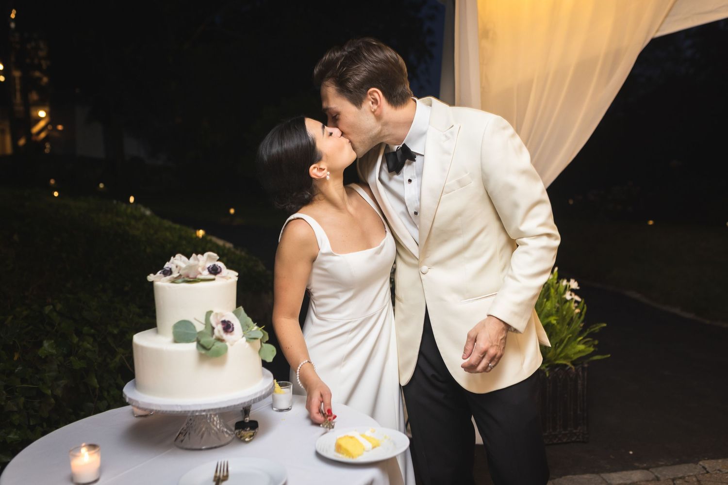 A bride and groom cut their elegant white tiered cake during their reception celebration.