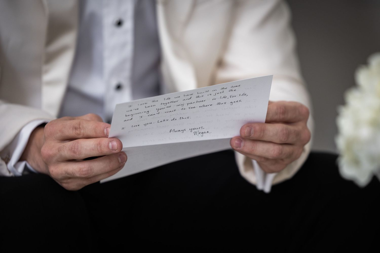 Hands holding handwritten wedding vows on white paper against a blurred background.